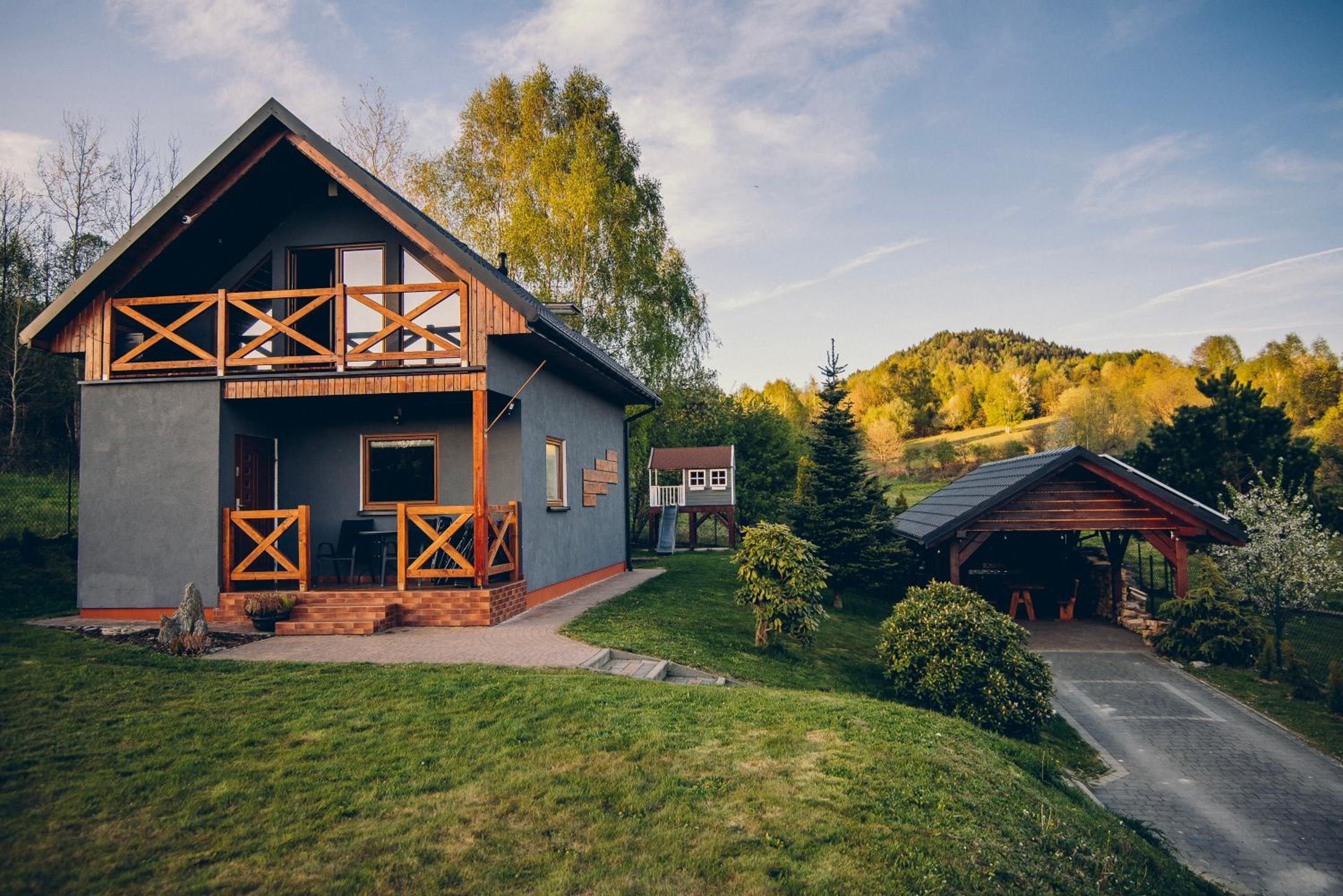 Zacisze Krzeszów — domek z drewnianymi balkonami w ogrodzie, z zielonymi wzgórzami w tle